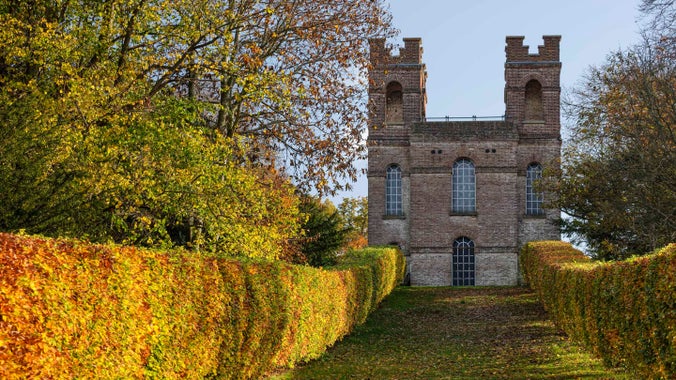 A view of the Belvedere tower surrounded by colourful orange and yellow foliage in autumn at Claremont Landscape Garden, Surrey